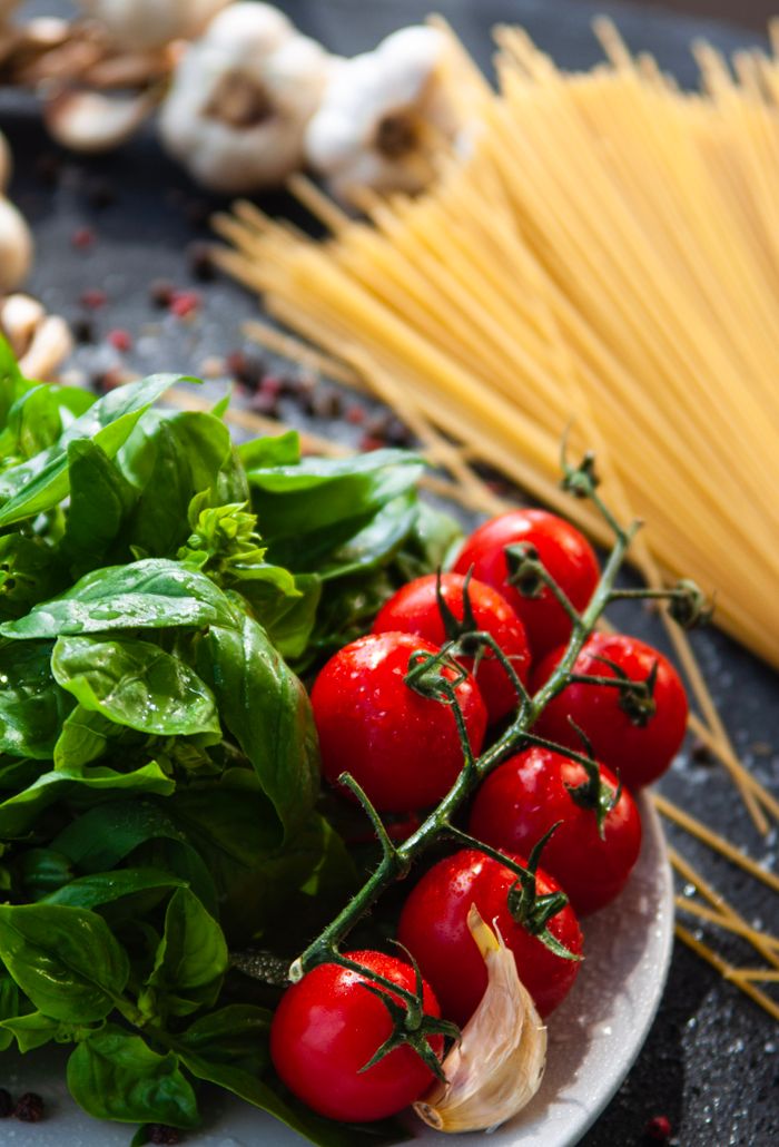 Close-up of fresh basil, vine tomatoes, and spaghetti for Italian pasta dishes.