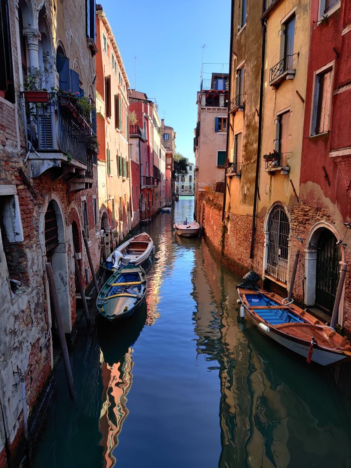 Scenic view of a tranquil canal in Venice with colorful buildings and boats reflecting in the water.